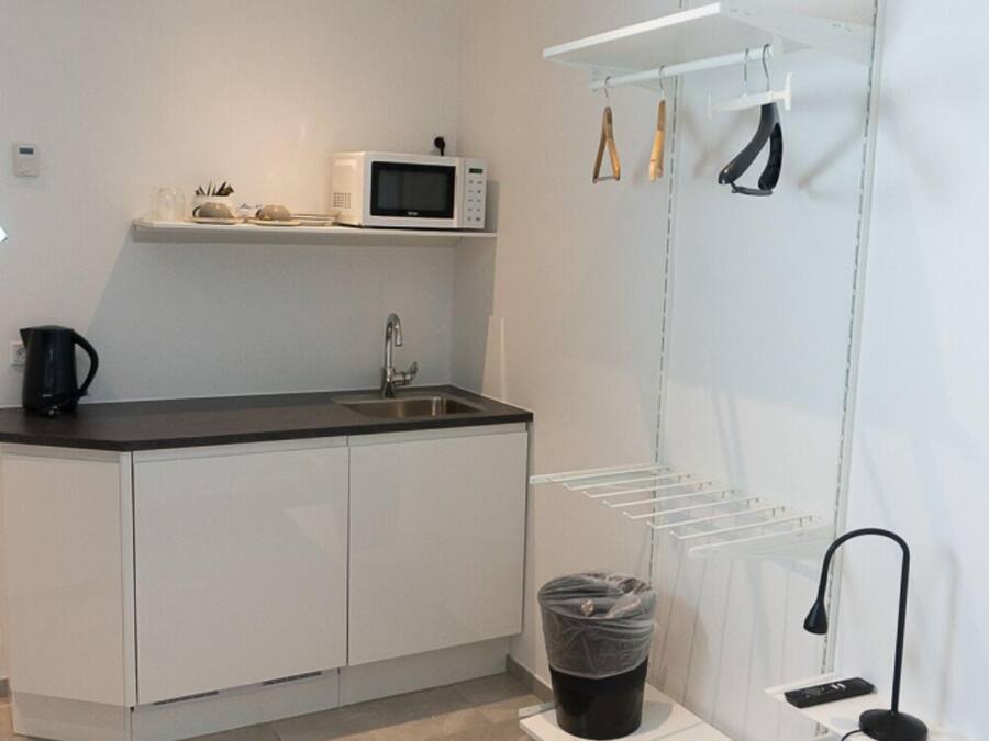 A modern kitchen with white cabinets, a black countertop, a microwave, a kettle, a sink, and a drying rack.