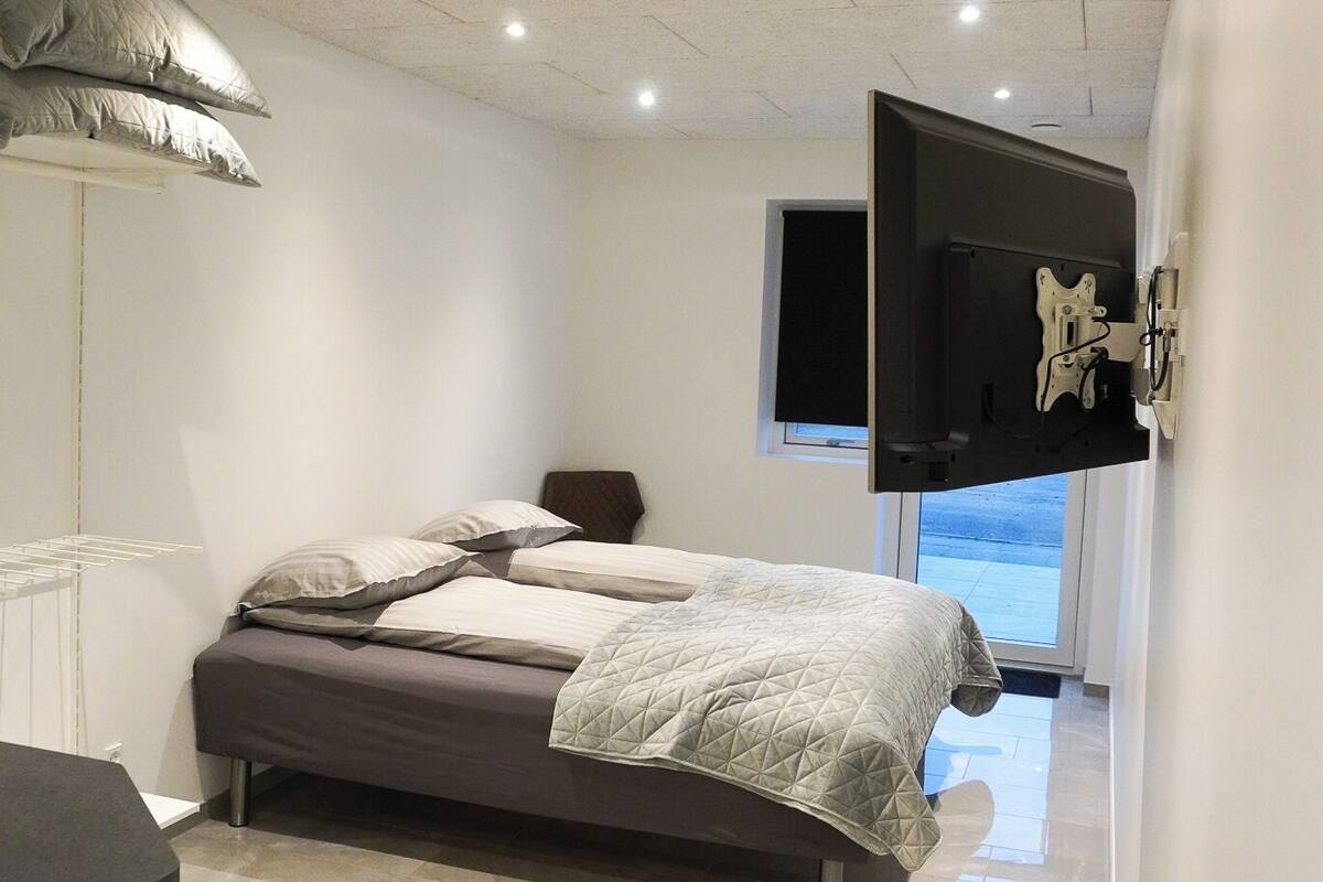 A bedroom with a bed, a mounted TV, and a window.