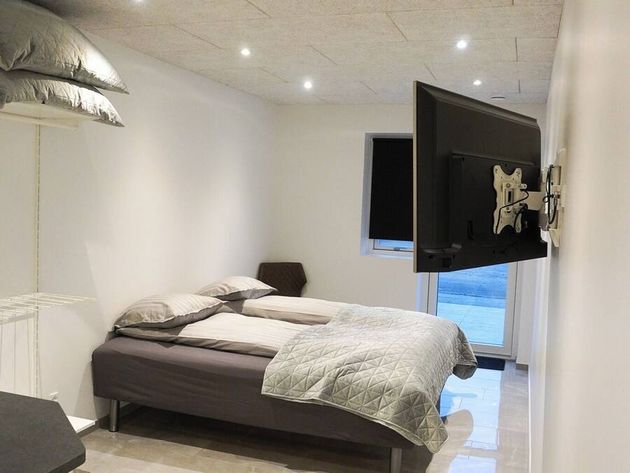 Une chambre à coucher avec un lit, un téléviseur fixé au mur et une fenêtre.
