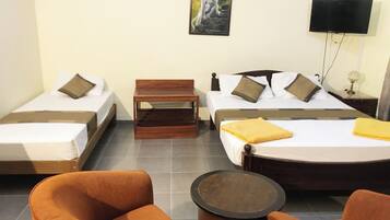 Habitación de hotel con dos camas individuales, una cama doble, un banco de madera, dos sillones naranja y una pequeña mesa redonda.