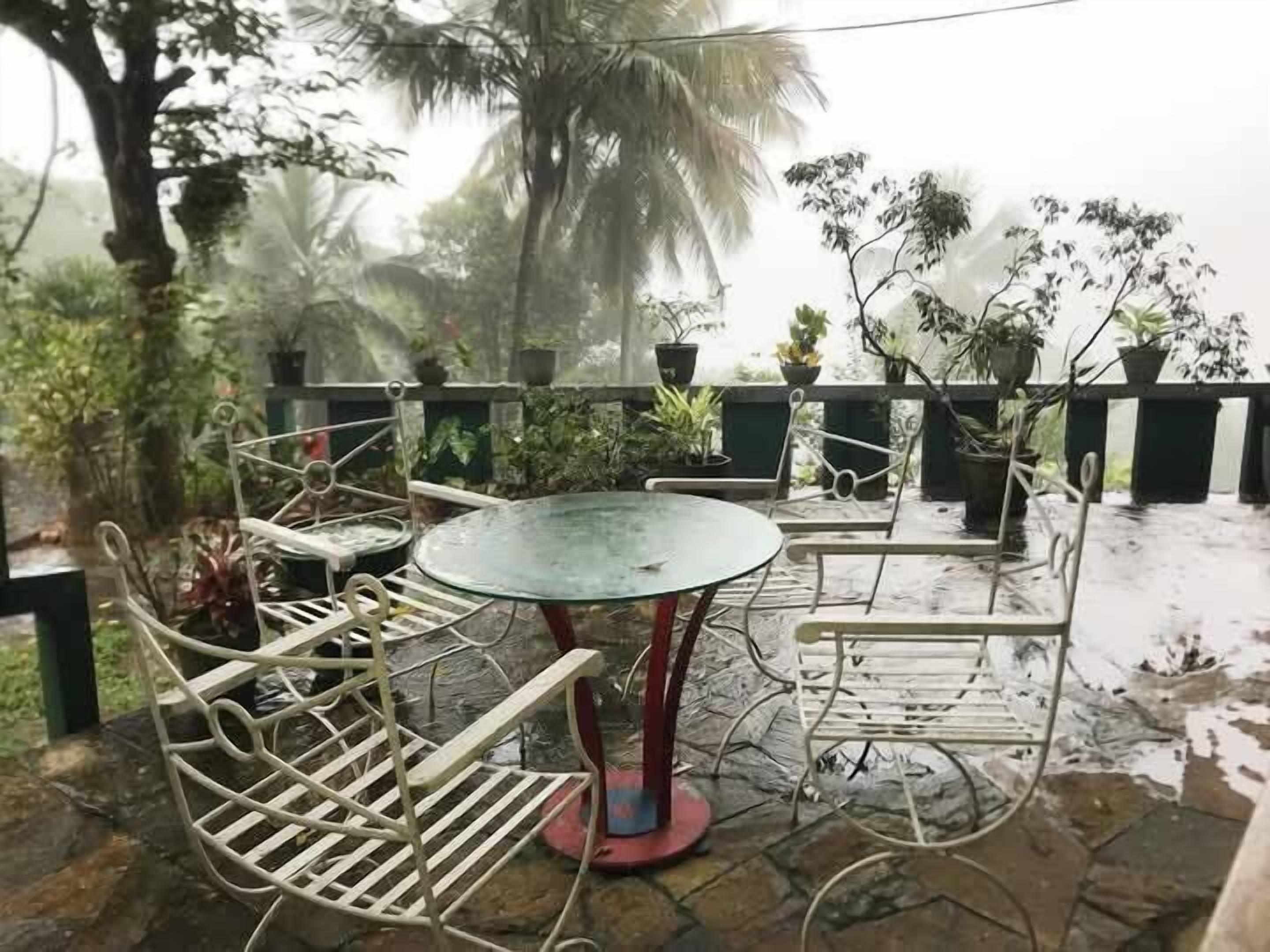Eine Terrasse im Freien mit einem runden Tisch und Metallstühlen, umgeben von Blumentöpfen und einem Steinboden.