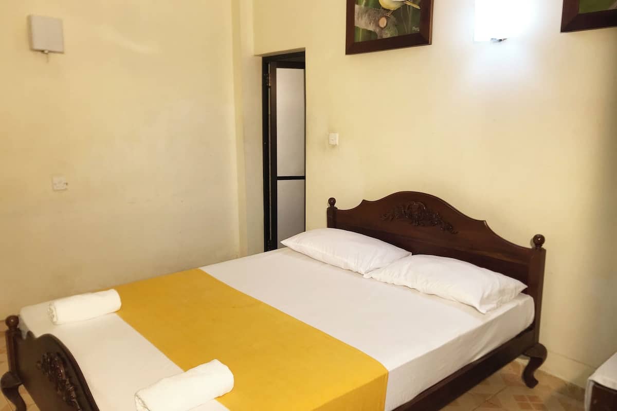 A single bed with a wooden headboard, white and yellow bedding, and a white towel on the footboard.