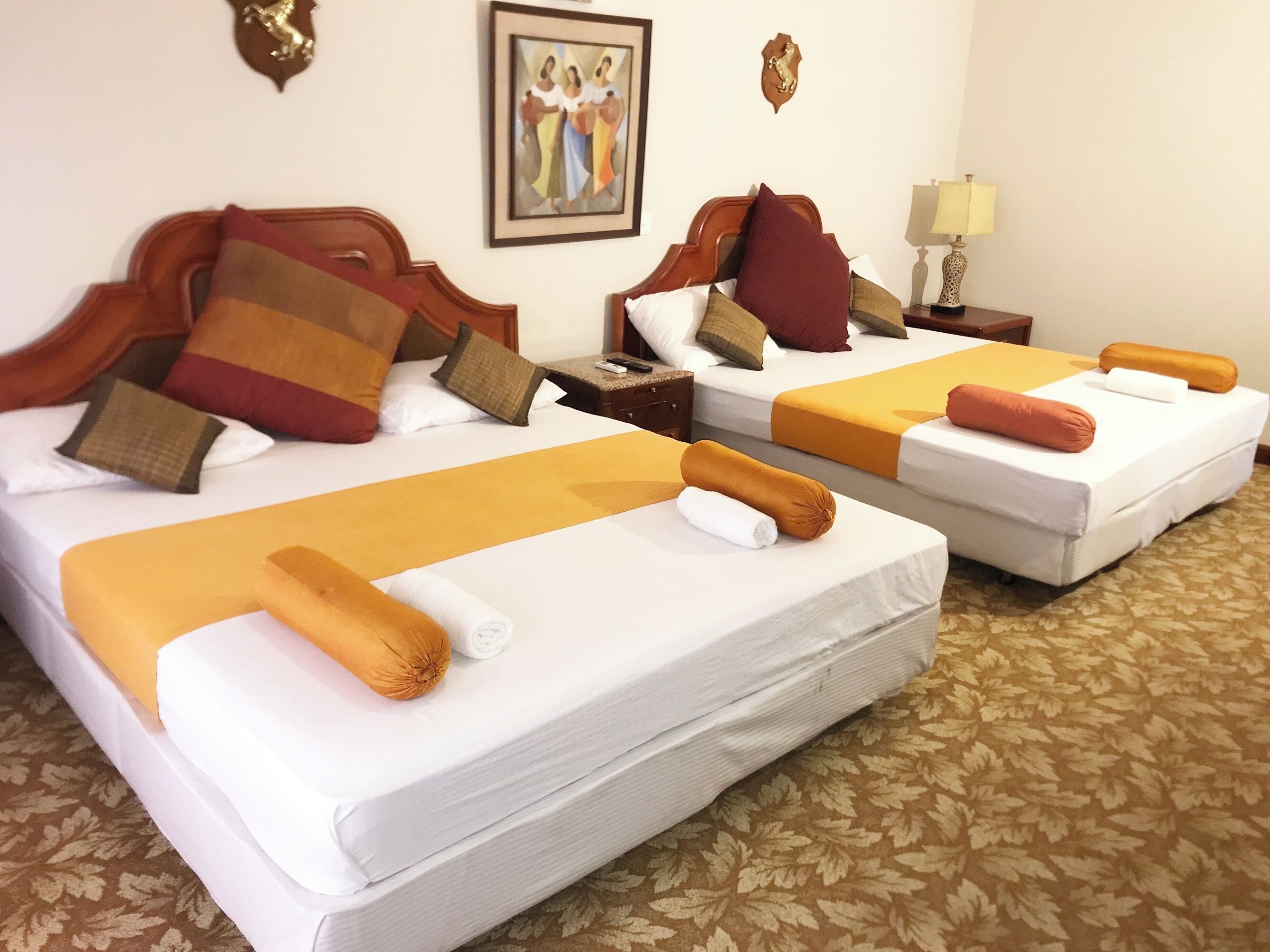 Duas camas de casal com lençóis brancos e cabeceiras marrons, um quadro emoldurado na parede e um tapete estampado.