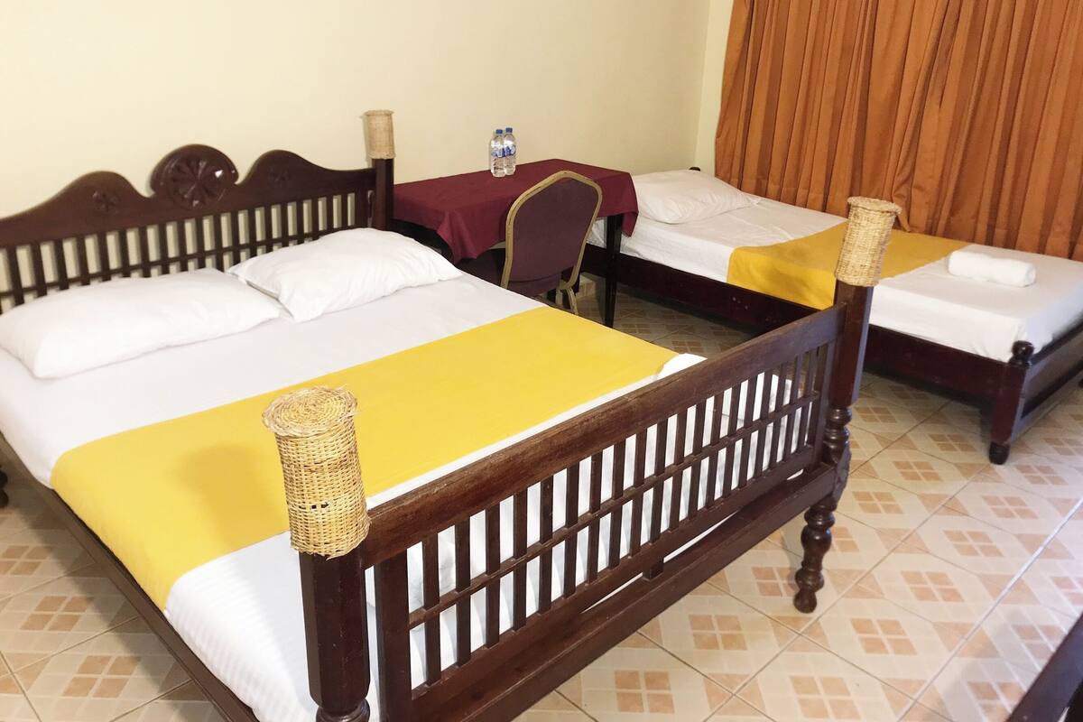 A hotel room with two beds, each with a wooden headboard and a yellow bedspread. There is a small table with a red tablecloth and a bottle of water on it.