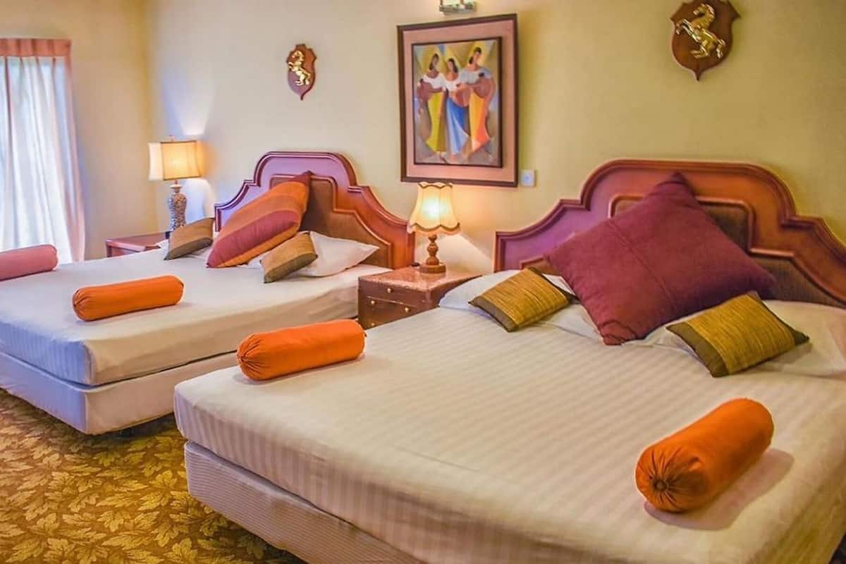 A hotel room with two beds, each with orange and purple pillows, a nightstand with a lamp, and a painting on the wall.