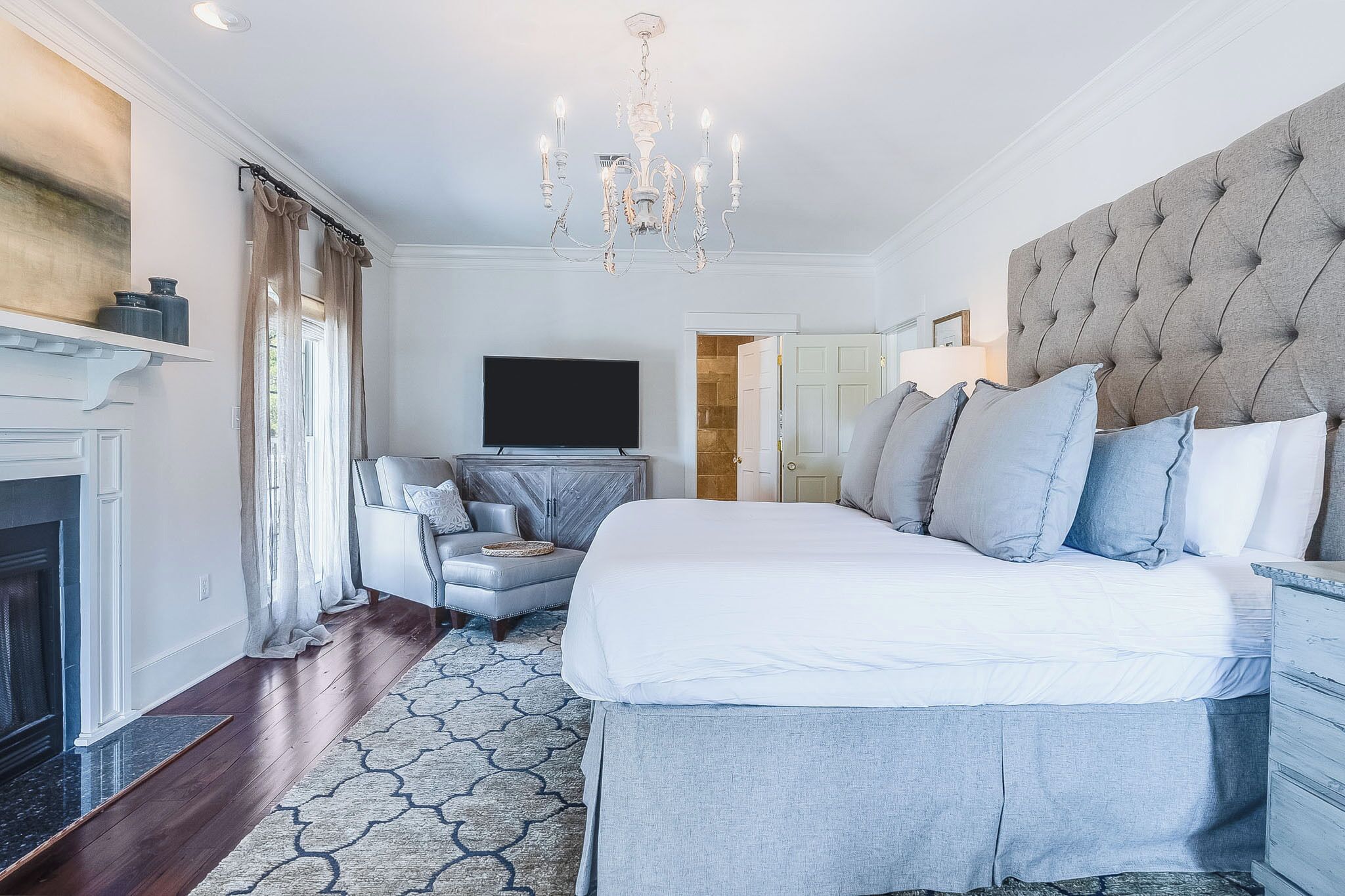 Un dormitorio con una cama grande, un televisor montado en la pared, una chimenea y un candelabro.