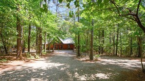 Une cabane entourée d’une forêt, avec un chemin de gravier menant à celle-ci.