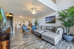 A modern living room with a sectional sofa, a ceiling fan, and a large potted plant.