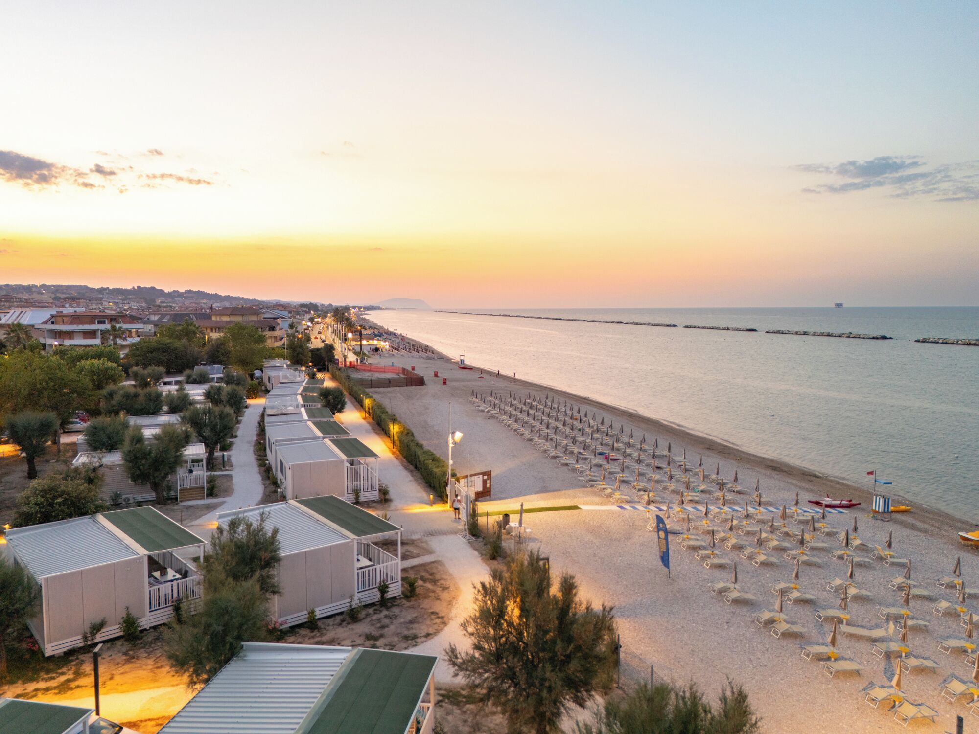 A beachside hotel with rows of beach chairs and umbrellas, a sandy beach, and a view of the sea.