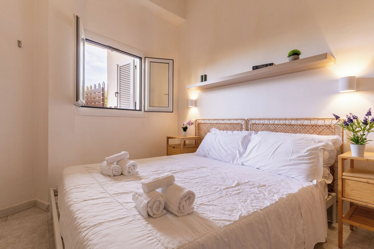Un letto rifatto con cura, asciugamani arrotolati, un comodino con una lampada e uno scaffale sopra il letto.