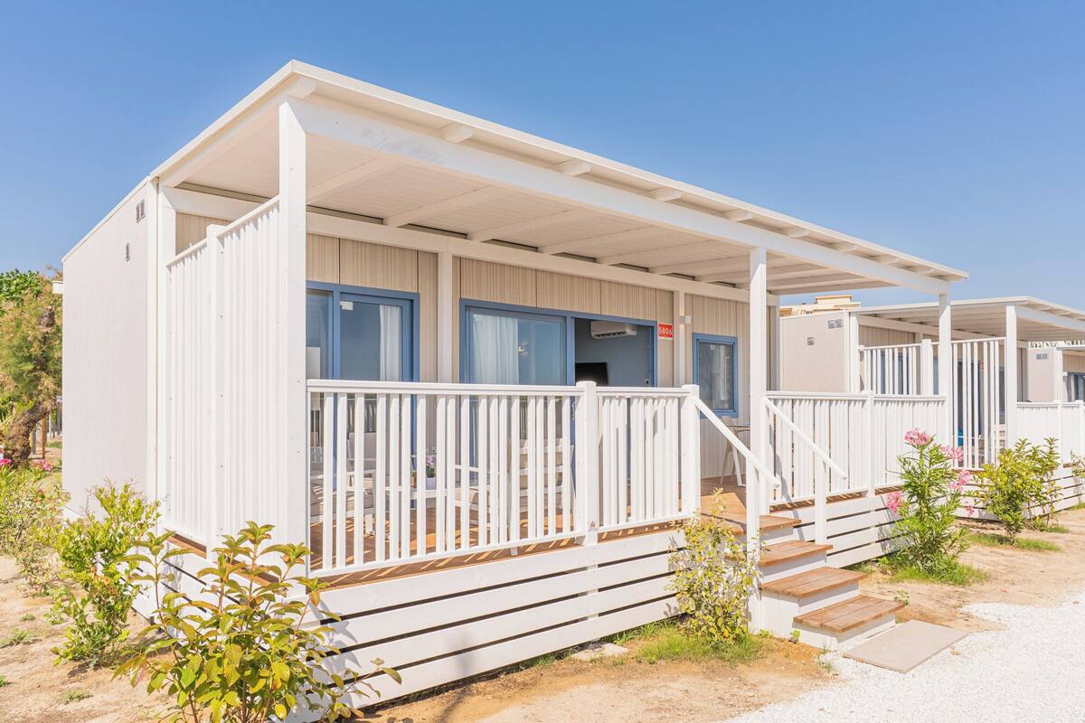 Une maison mobile de plain-pied dotée d’une véranda, d’une petite terrasse et d’un escalier menant à l’entrée.