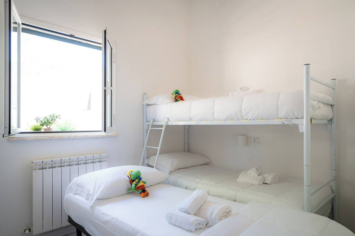 Une chambre avec un lit superposé, une fenêtre, un radiateur et un jouet sur le lit du bas.