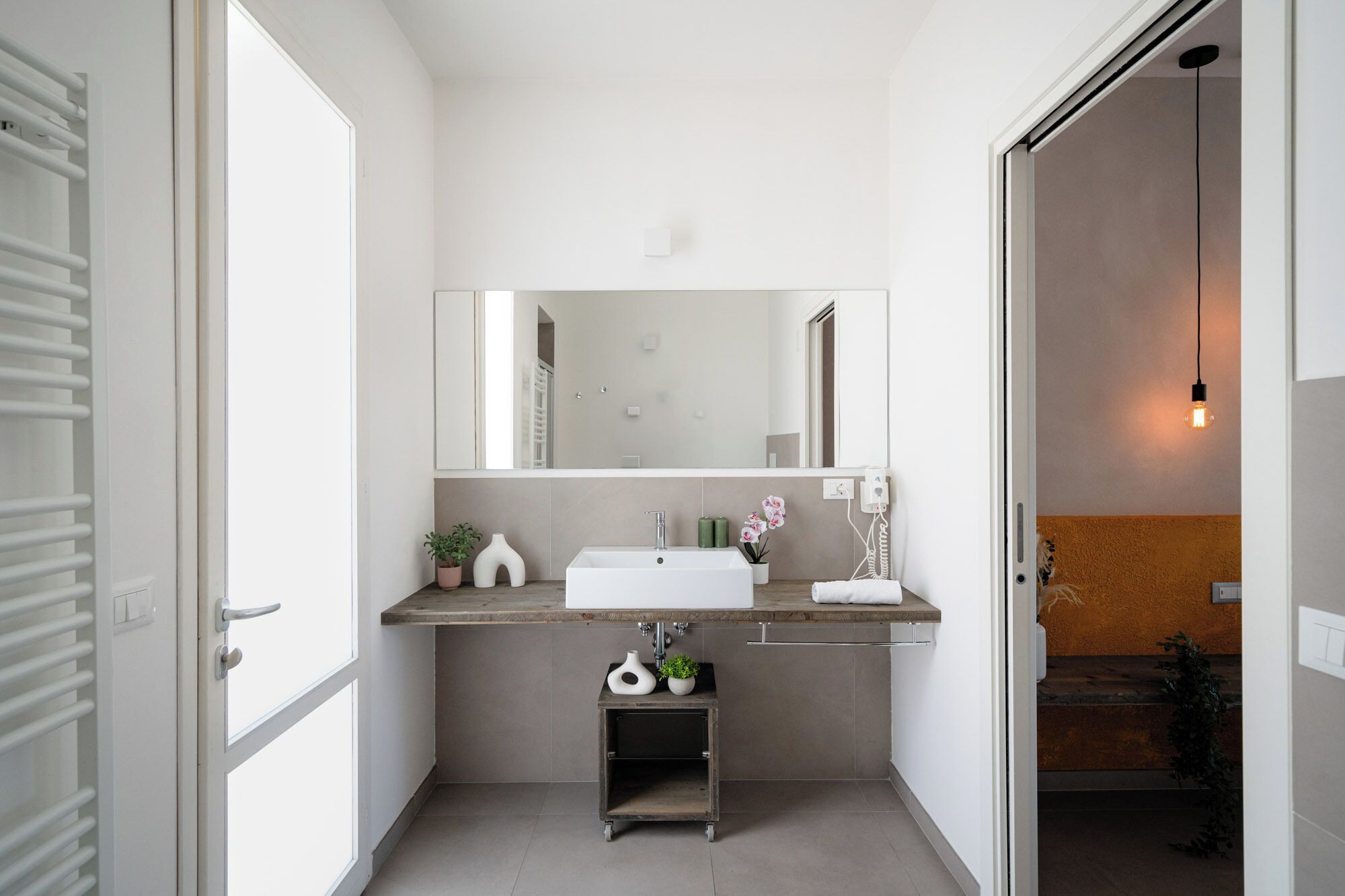 Een moderne badkamer met een grote spiegel, een witte wastafel en een klein plankje met decoratieve objecten.