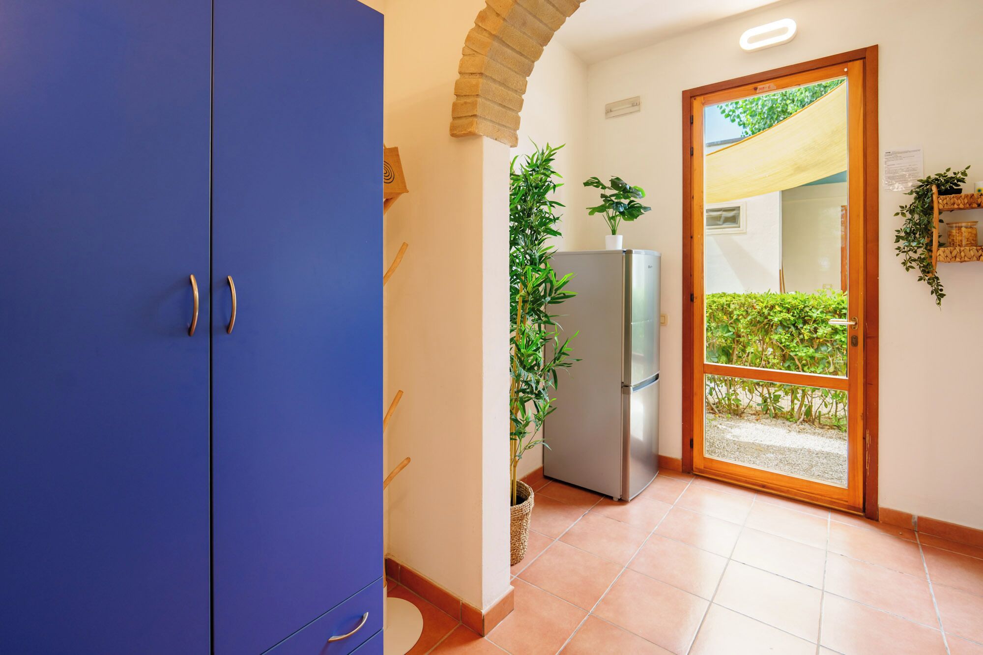 A hallway with a blue cabinet, a refrigerator, and a door leading outside.