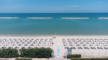 A beach with rows of umbrellas and sun loungers, a lifeguard tower, and a clear view of the sea.