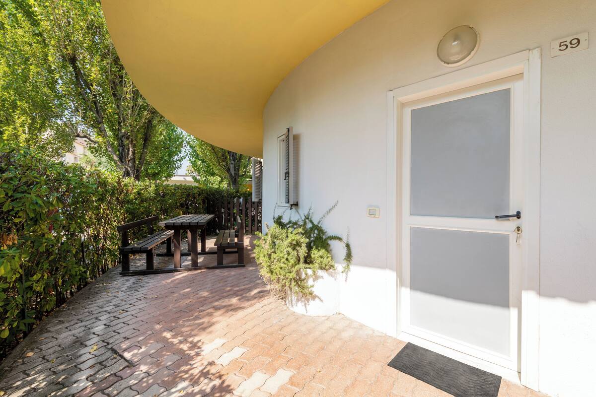 Un patio abrité avec un banc en bois, une plante en pot et une porte portant le numéro 59.