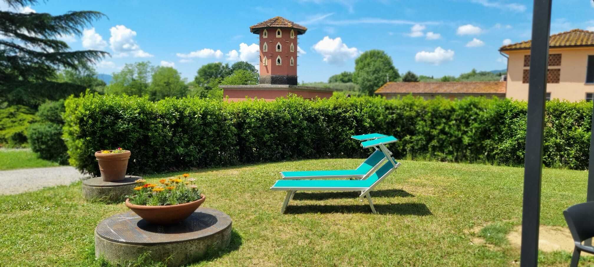 Um jardim com um banco, uma torre pequena e um edifício ao fundo.