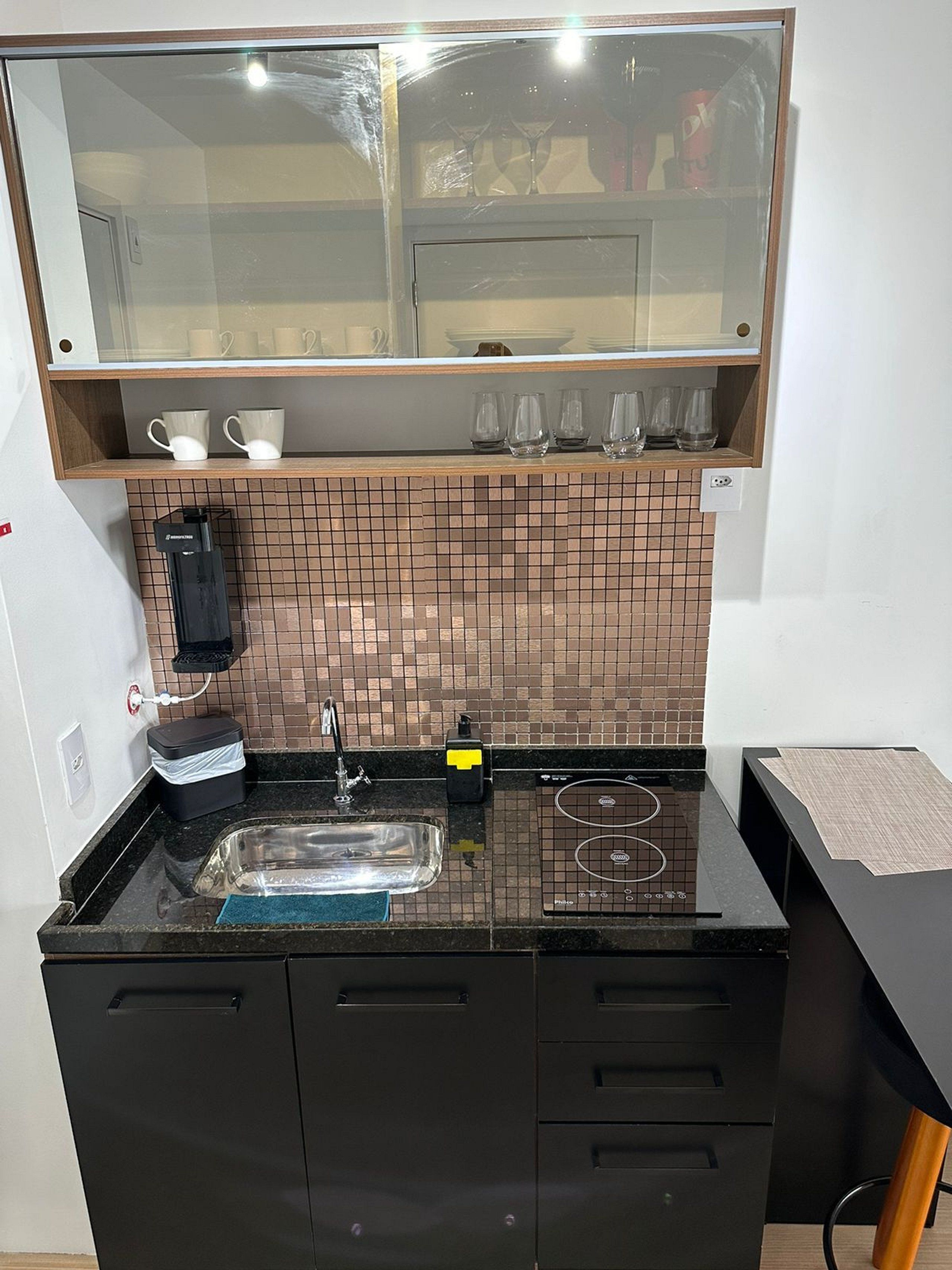 A modern kitchen with a black countertop, a sink, a coffee machine, and a tiled backsplash.