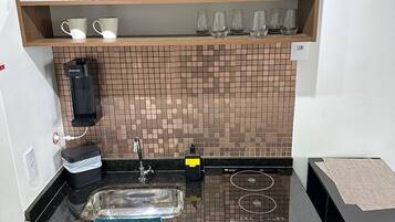 A modern kitchen with a black countertop, a sink, a coffee machine, and a tiled backsplash.