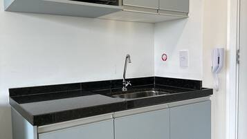 A kitchen with a black countertop, grey cabinets, a stainless steel sink, and a microwave.