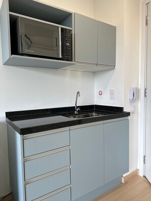 A kitchen with a black countertop, grey cabinets, a stainless steel sink, and a microwave. - TrevizZo Borba Gato (São Paulo)