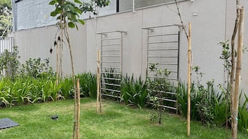 Un bâtiment moderne doté d’un toit plat, d’un mur en béton et d’une cour verdoyante agrémentée de plantes de bambou et d’une clôture en métal.