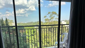 A hotel room with a bed, two towels, a balcony with a chair, and a view of greenery and buildings. - TrevizZo Borba Gato (São Paulo)