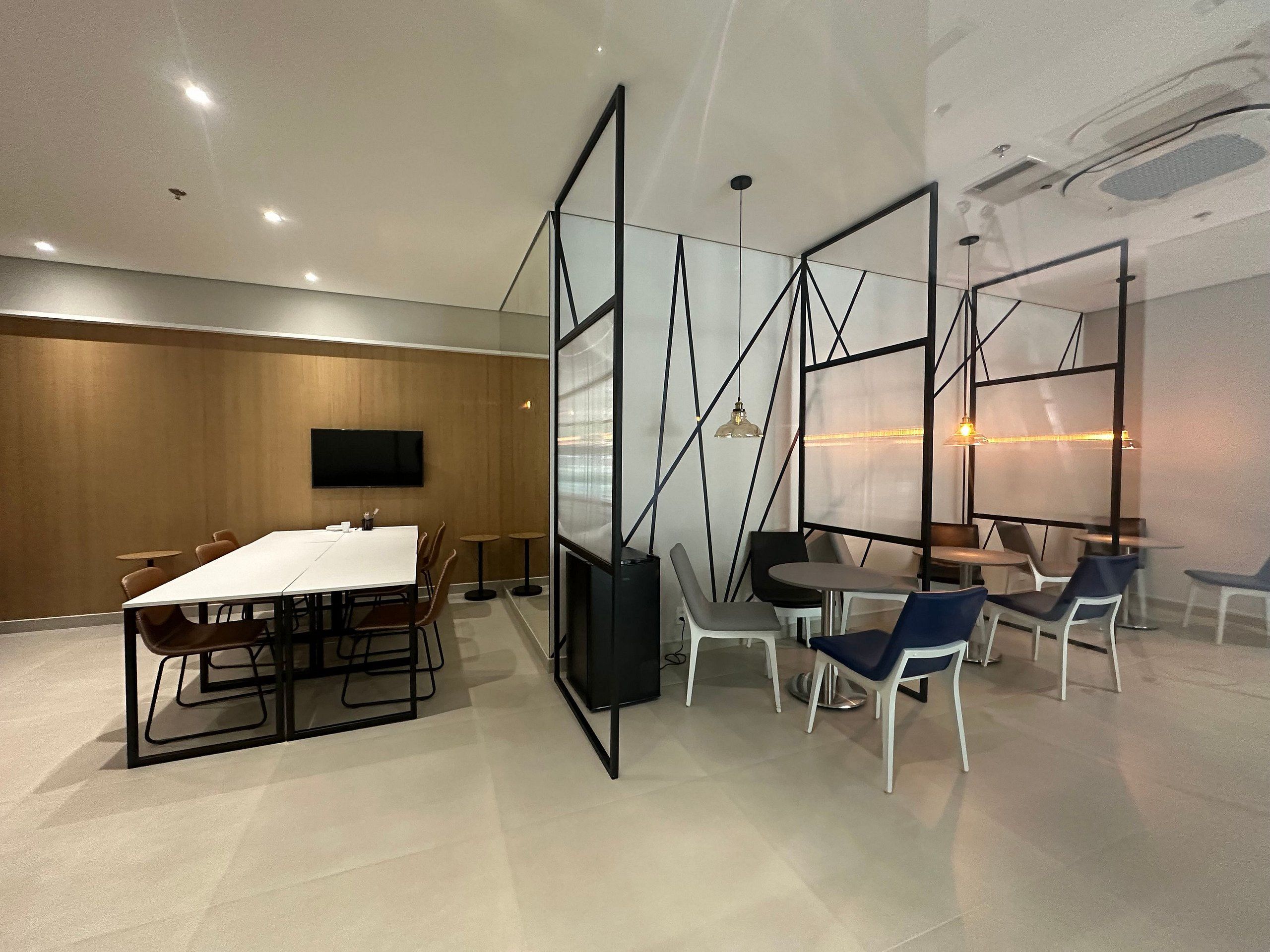 Une salle de réunion moderne, dotée d’une longue table, de chaises, d’un téléviseur et de cloisons en verre.