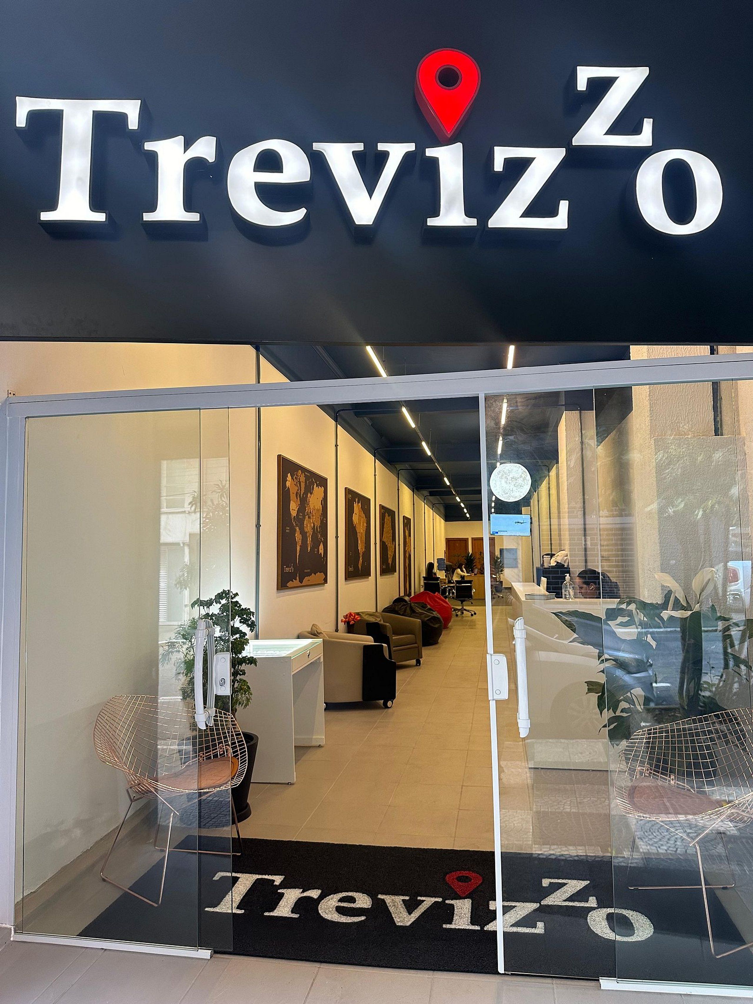 L’entrée d’un hôtel appelé Treviso, avec un comptoir d’accueil, un espace salon et des cartes du monde accrochées aux murs.