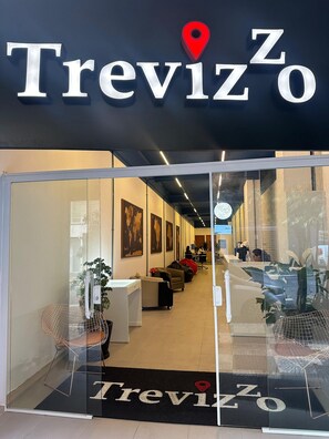 La entrada de un hotel llamado Treviso, con un mostrador de recepción, zona de estar y mapas del mundo en las paredes.