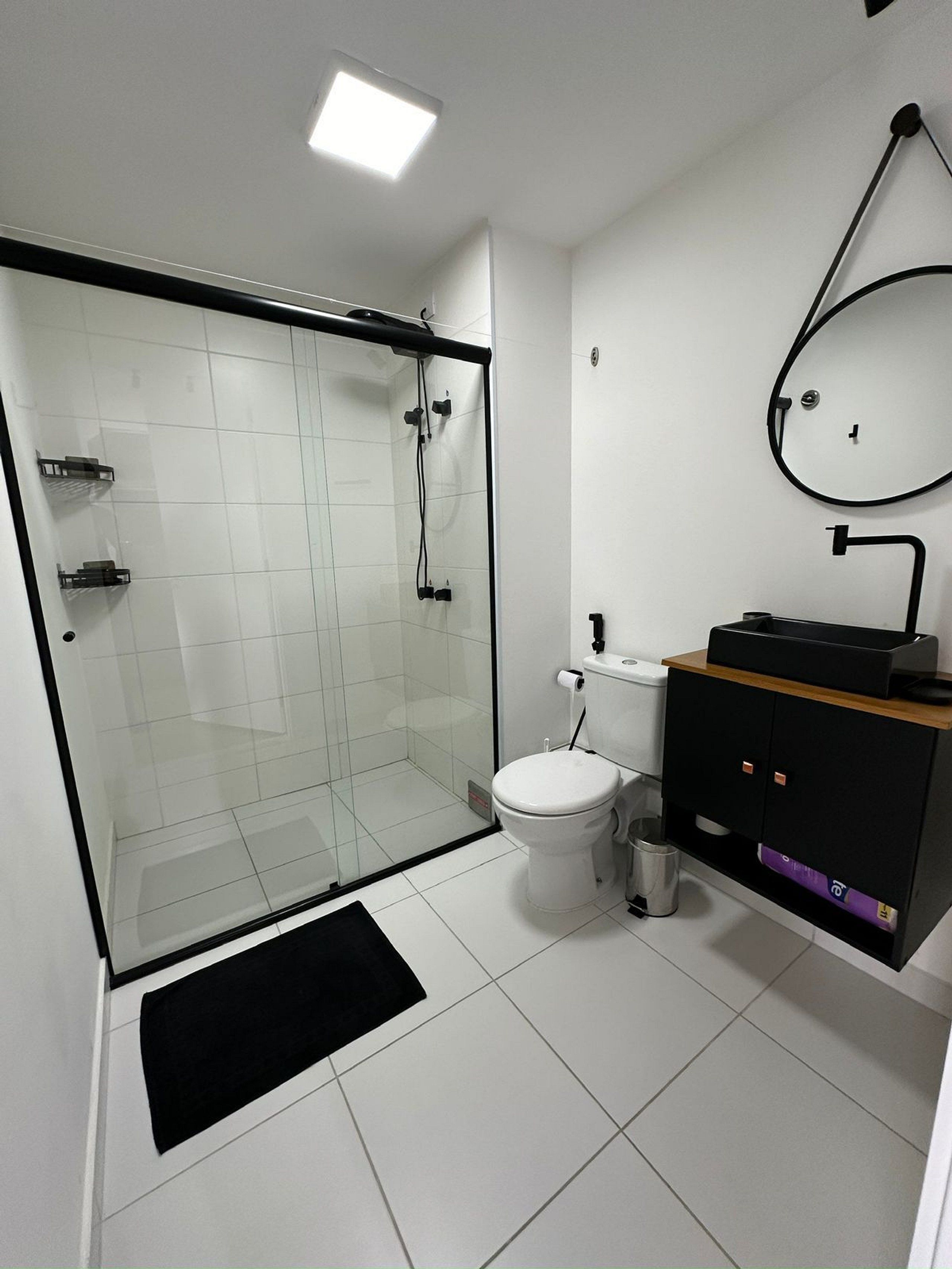 Un baño moderno con cabina de ducha de vidrio, inodoro y lavamanos con mueble negro.