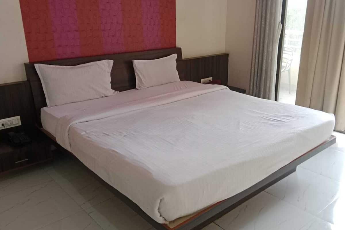 A large bed with a wooden headboard, white bedding, and a power outlet on the left side.