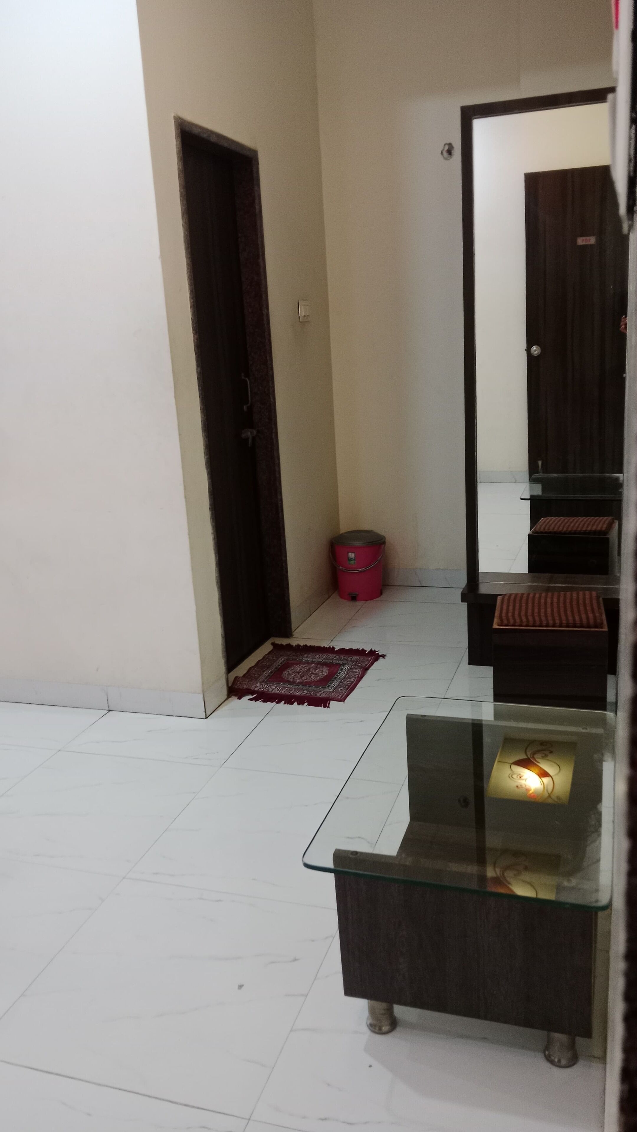 A room with a glass coffee table, a red trash bin, a patterned rug, and a dark wooden door.