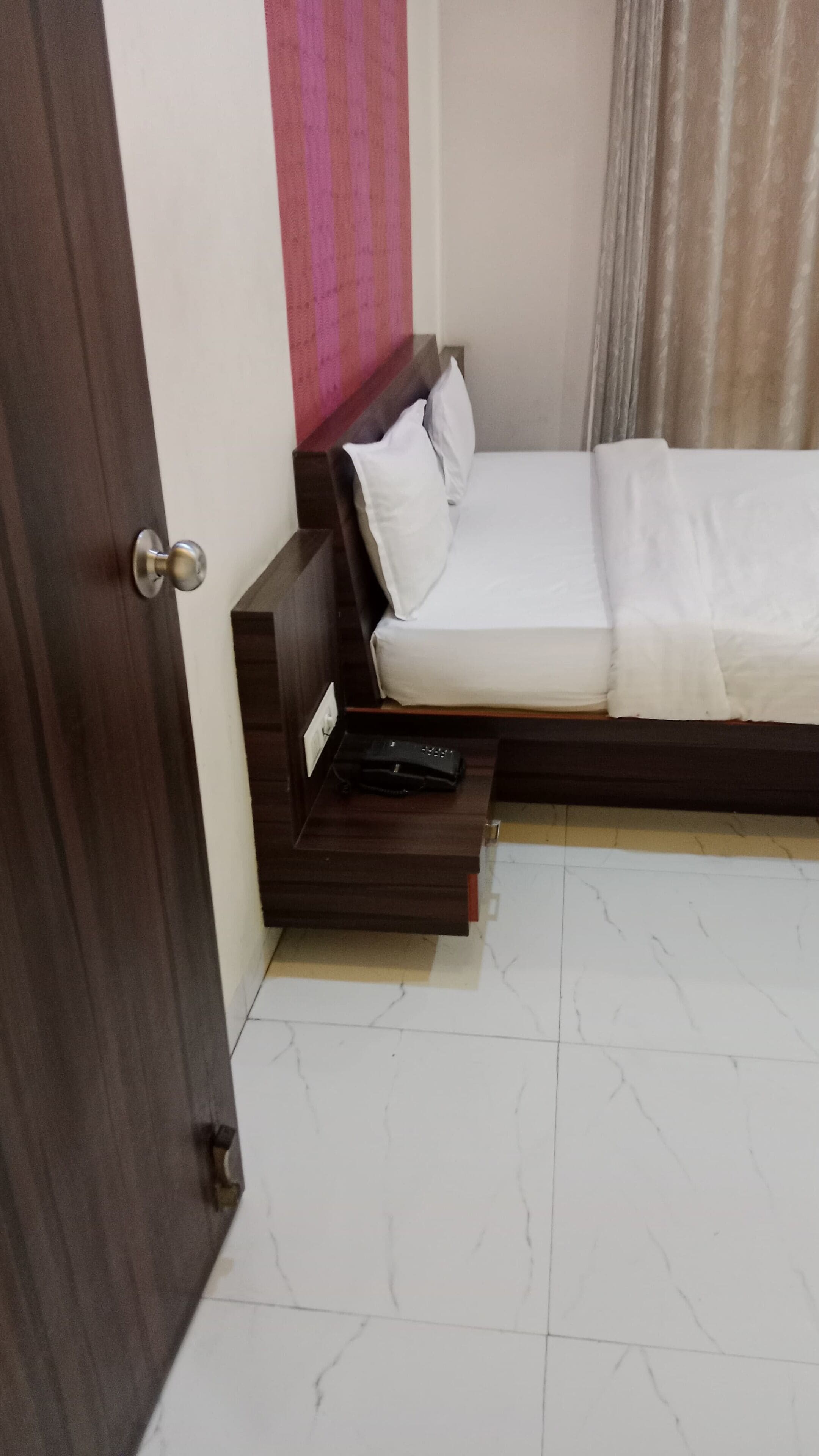 A bedroom with a bed, a nightstand, a power outlet, and a door.