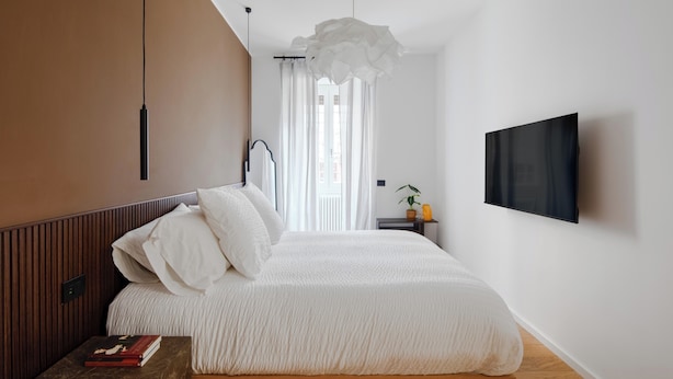 Une chambre à coucher moderne, avec un lit, une table de chevet, un téléviseur fixé au mur et une fenêtre avec des rideaux.
