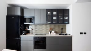 Une cuisine moderne avec un réfrigérateur, un four à micro-ondes et un four, tous de couleur noire, des armoires grises et un plan de travail blanc.