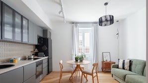 Une cuisine moderne avec des meubles gris, une table à manger en bois avec des chaises, et un canapé vert dans l’espace salon.