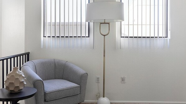 A room with a grey armchair, a floor lamp, and a vase on a small table.
