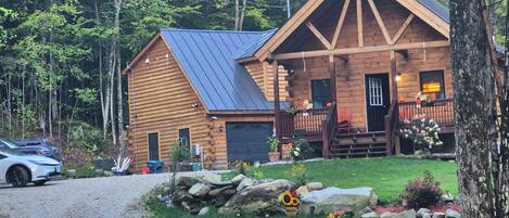 A log cabin with a porch, a garage, and a driveway leading to a parked car.