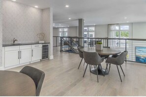A modern kitchen with white cabinets and a marble backsplash, a dining area with a round table and chairs, and a balcony with a railing. - Landing | Amazing 2BD, Pool, Yoga Studio (Direct Placeholder City)