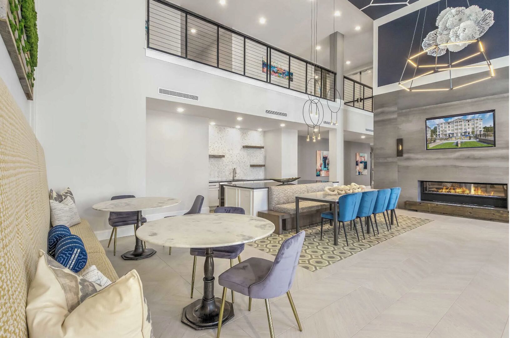 Un vaste espace de vie doté d’un haut plafond, d’une cheminée et d’un coin repas avec des chaises bleues.
