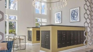 En rymlig hotellobby med en central receptionsdisk, modern hängande belysning och stora fönster som släpper in naturligt ljus.