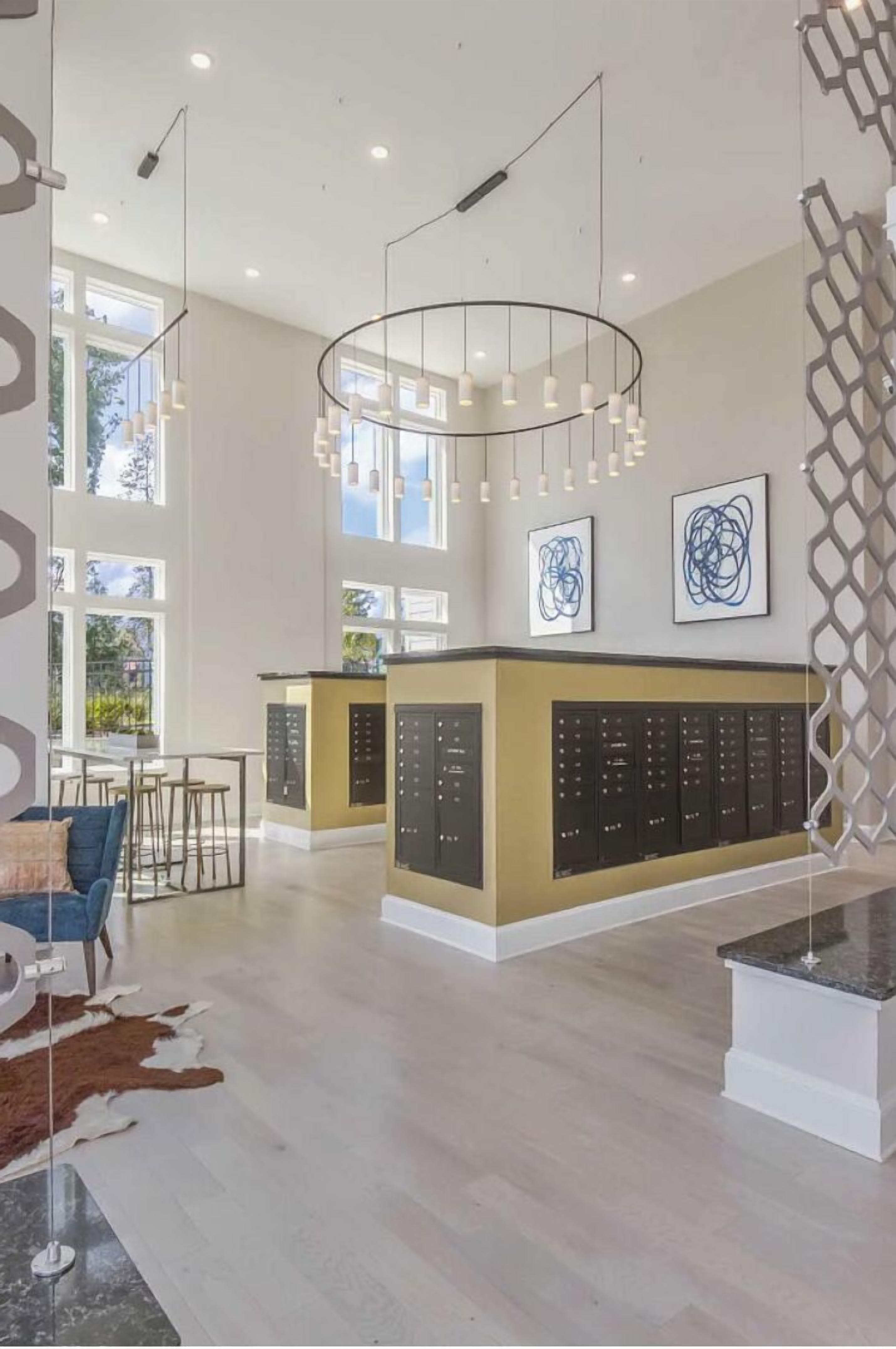 Un hall d’hôtel spacieux, doté d’un comptoir d’accueil central, d’un éclairage moderne suspendu et de grandes fenêtres laissant entrer la lumière naturelle.