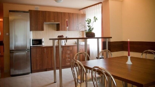Kompakti keittiö, jossa on puiset kaapit, ruostumattomasta teräksestä valmistettu jääkaappi, mikroaaltouuni sekä ruokapöytä tuoleineen.