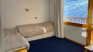 A room with a bed, a small table, a window with curtains, and a view of a snowy landscape. - Studio with balcony in Plagne Village (Plagne Village)