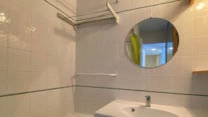 A bathroom with white tiles, a round mirror, a white sink, and a bathtub. - Studio with balcony in Plagne Village (Plagne Village)