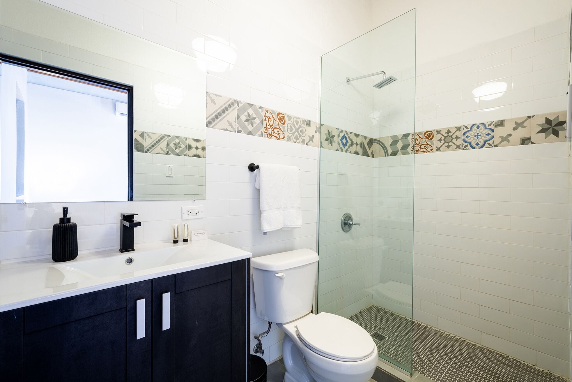 A modern bathroom with a glass shower enclosure, white tiles, and a black vanity.