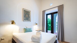 Habitación de hotel con una cama grande, dos lámparas fijadas a la pared, una obra de arte enmarcada y vistas a zonas verdes a través de una puerta corrediza.