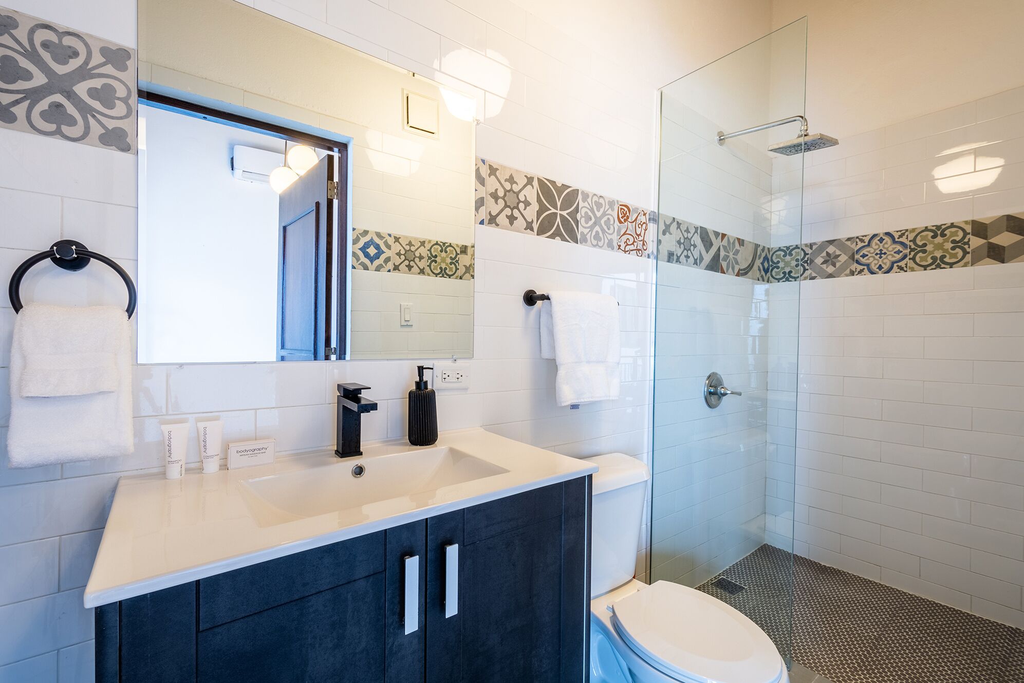 A modern bathroom with a glass shower enclosure, a white toilet, and a vanity with dark cabinets.