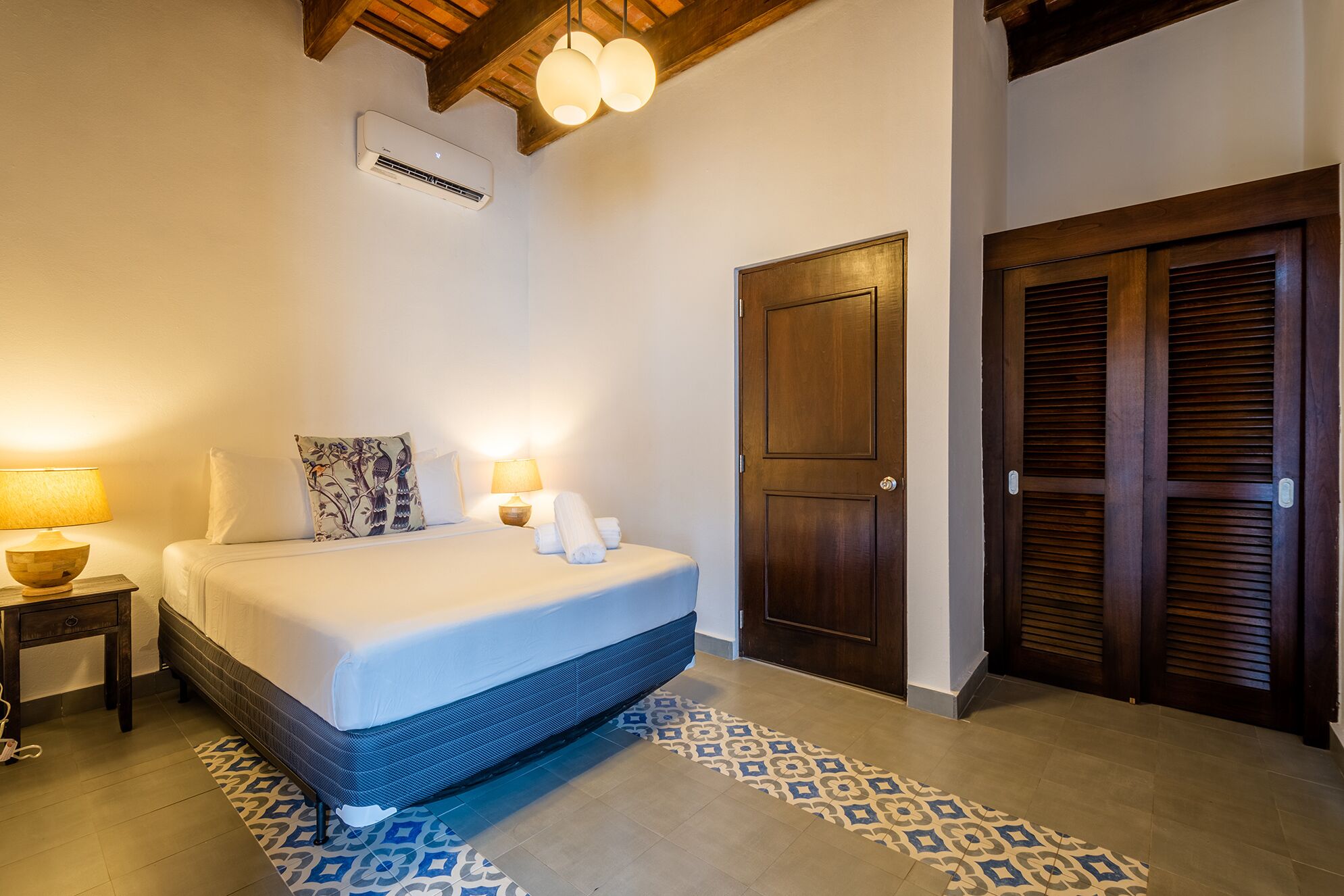 Une chambre à coucher avec un lit, des lampes de chevet, une porte en bois et un tapis à motifs.